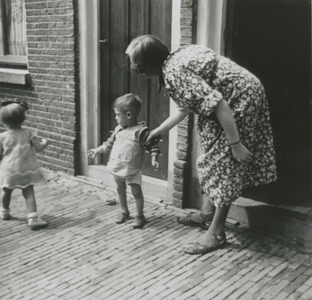 876885 Afbeelding van een onbekende moeder met twee kinderen bij de deuropening van hun woning op een onbekende locatie ...
